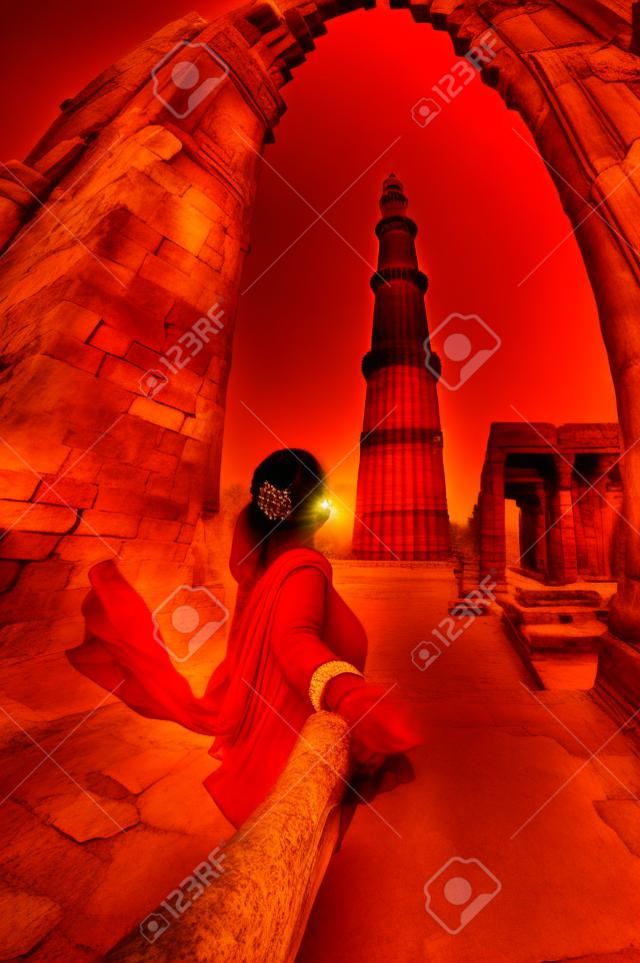 红色服装的男主角的女人用手Qutub Minar塔在印度的新德里