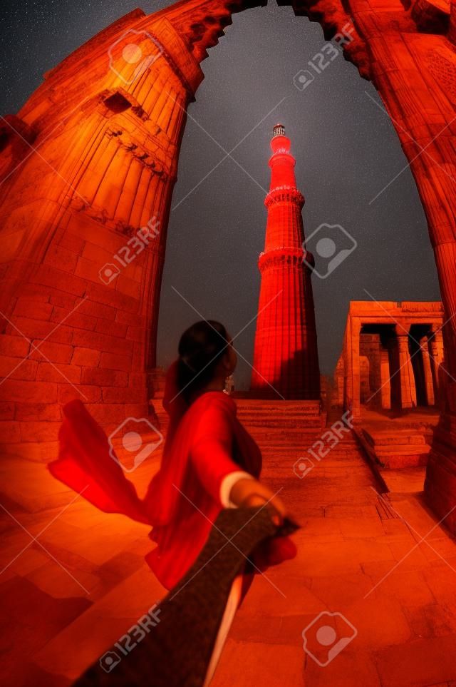 红色服装的男主角的女人用手Qutub Minar塔在印度的新德里