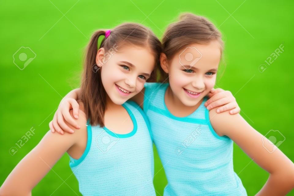 Happy preteen girls friendly hugging on green grass background