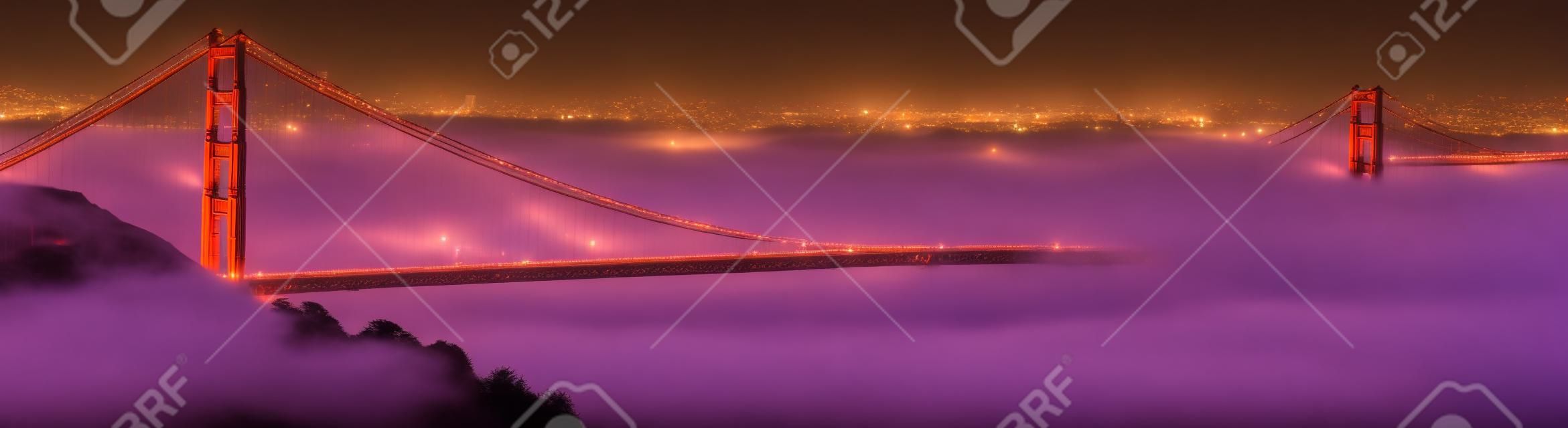 Fog rolls the Golden Gate Bridge at dusk. The city of San Francisco is in the background. Panoramic composition.