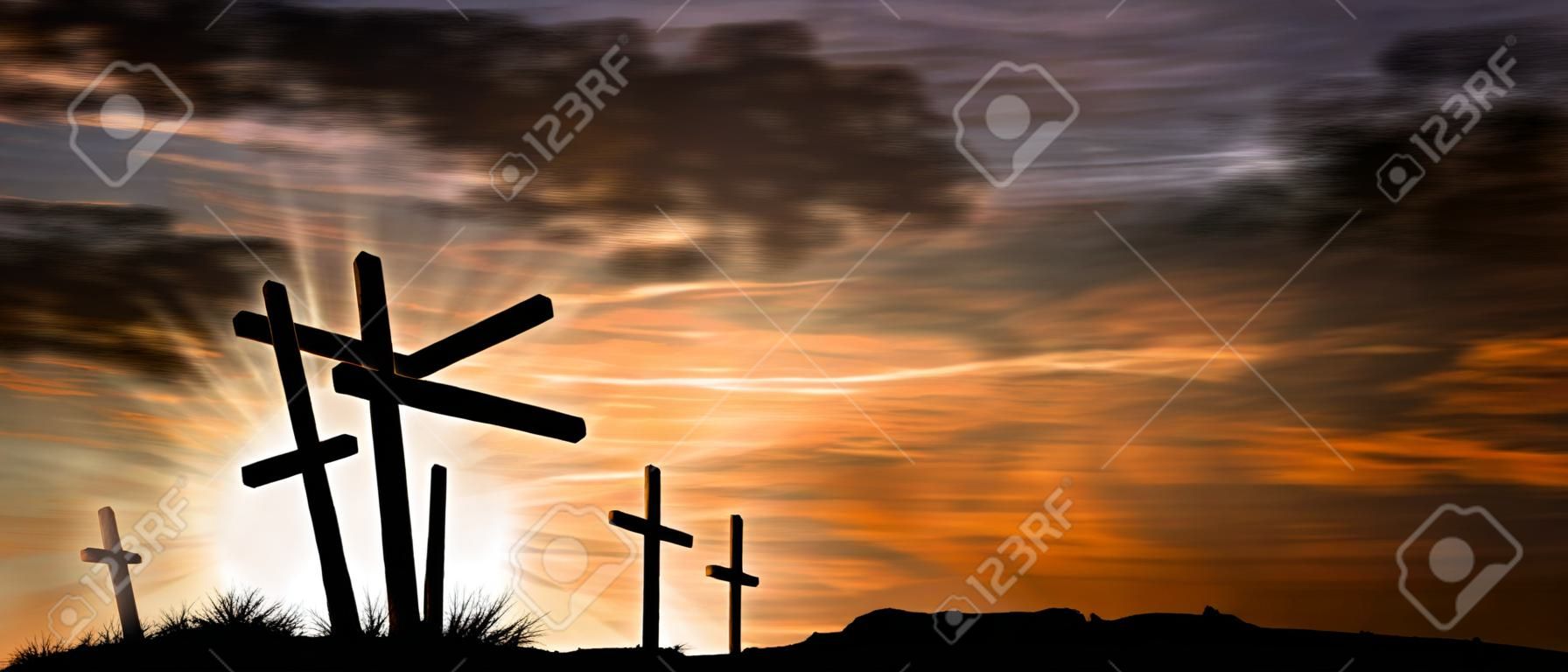Silhouette of three wooden crosses above the hill with dramatic sky and sun rays at sunset. Religious symbol of good friday