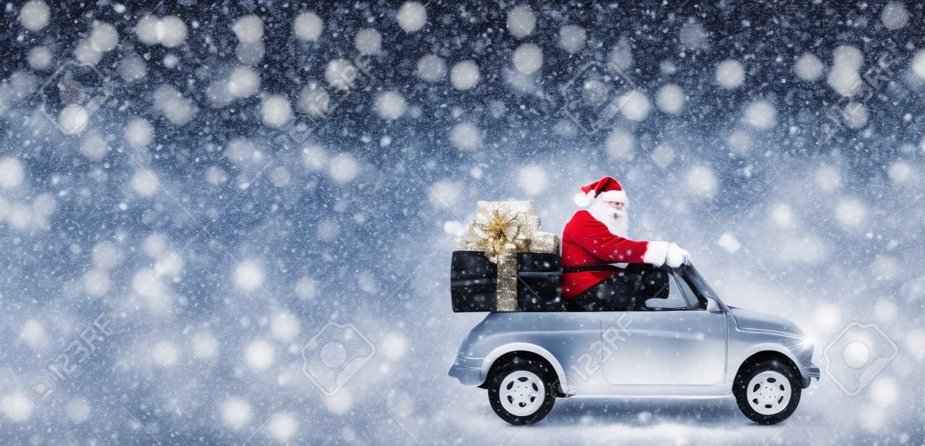 雪に覆われた灰色の背景でクリスマスまたは新年の贈り物を提供する車のサンタ クロース