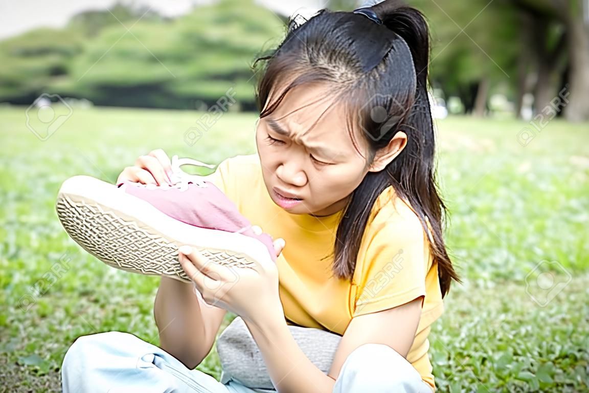 Asian female teenage is sniffing her sneakers,hold stinky shoe in her hand with disgust on her face,unpleasant smell because of hot weather or after exercise,child girl with bad smell,accumulated dirt