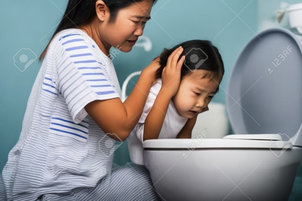 Sick asian child girl about to throw up,puking,vomiting into the toilet bowl,mother is taking care of her closely,suffering from indigestion,food poisoning,acute infectious diseases,gastritis problem