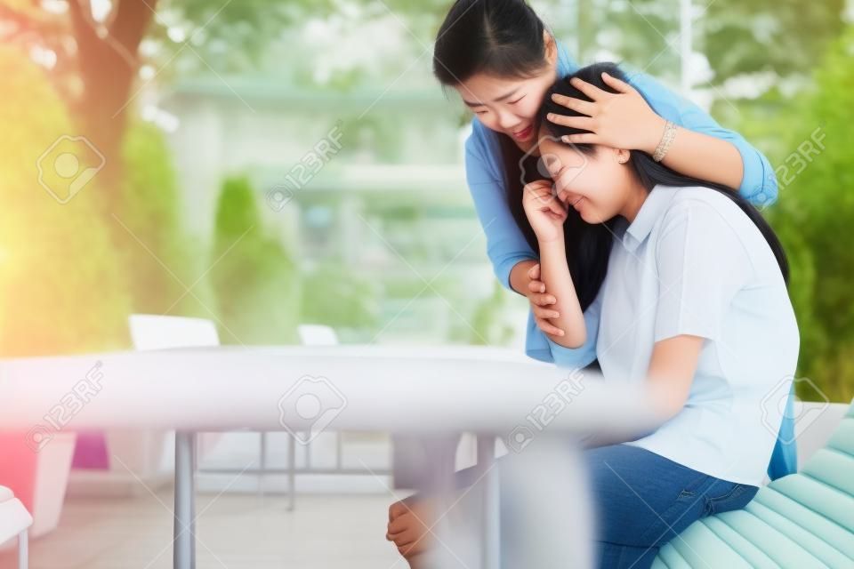 La donna asiatica sta abbracciando il conforto e la cura della figlia triste a scuola, una bambina depressa seduta a piangere, una madre amorevole che esprime empatia, parla è consolante, concetto di relazione