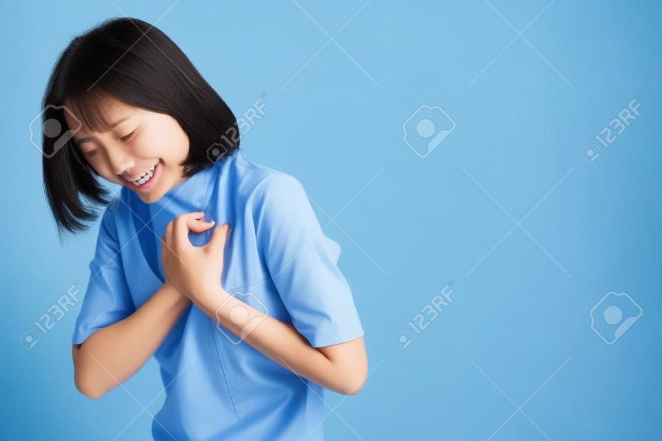 Asian woman was sick with chest pain and standing isolated over blue background. Health care concepts.