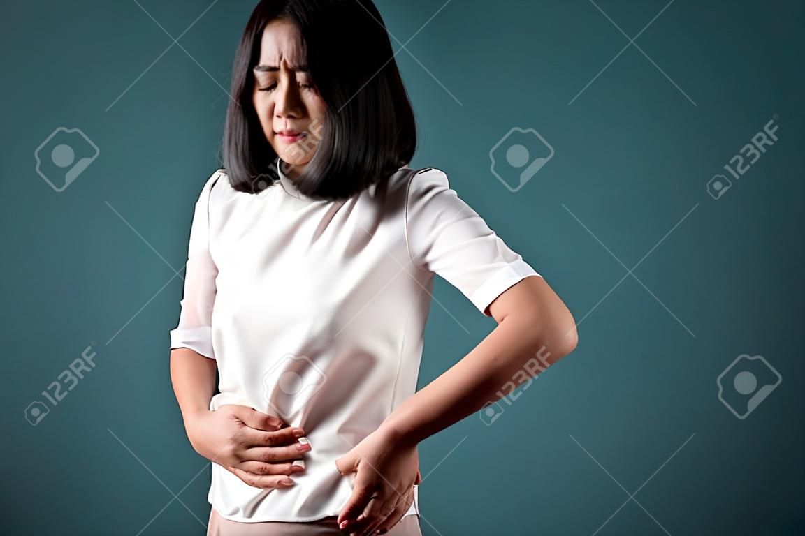 Asian woman was sick with stomach ache and standing isolated over blue background. Health care concepts.