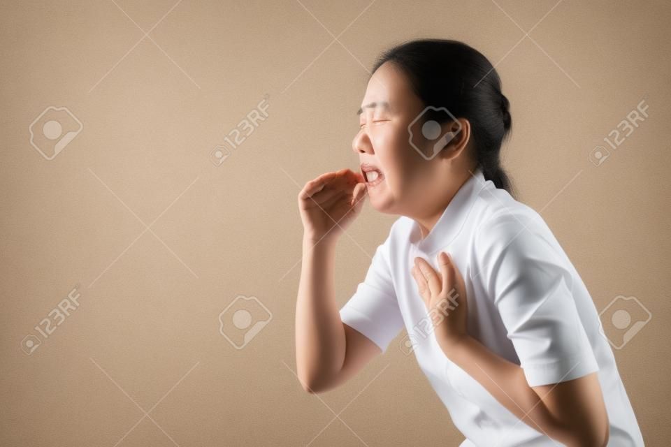 Asian woman was sick with sore throat, coughing sneezing and standing isolated on beige background. Low key