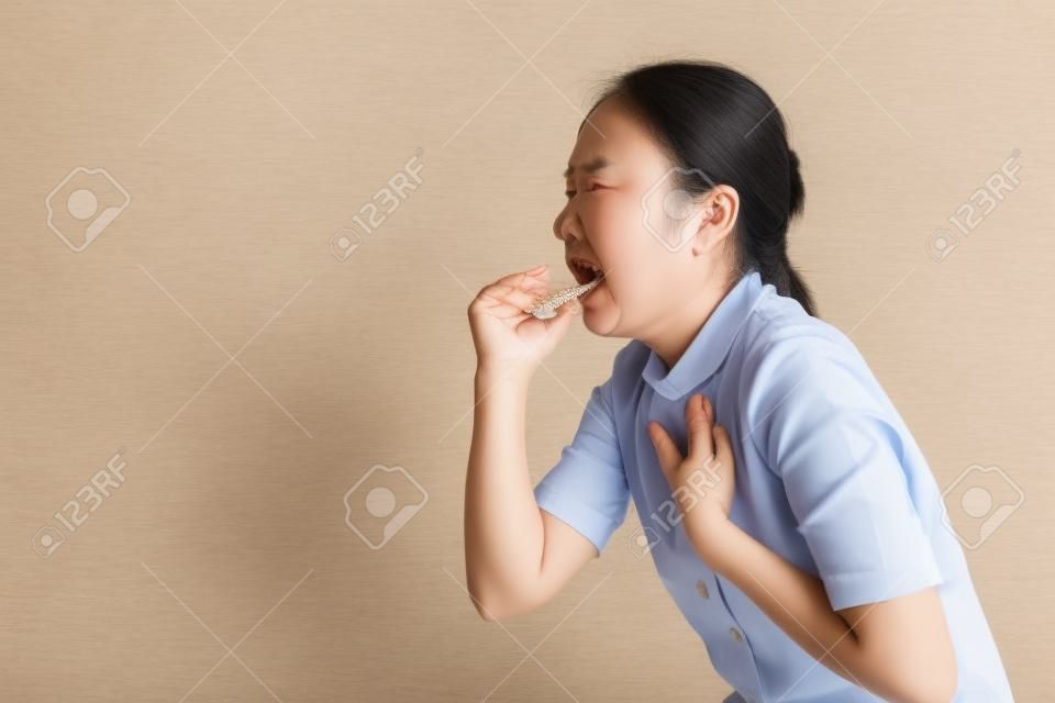 Asian woman was sick with sore throat, coughing sneezing and standing isolated on beige background. Low key