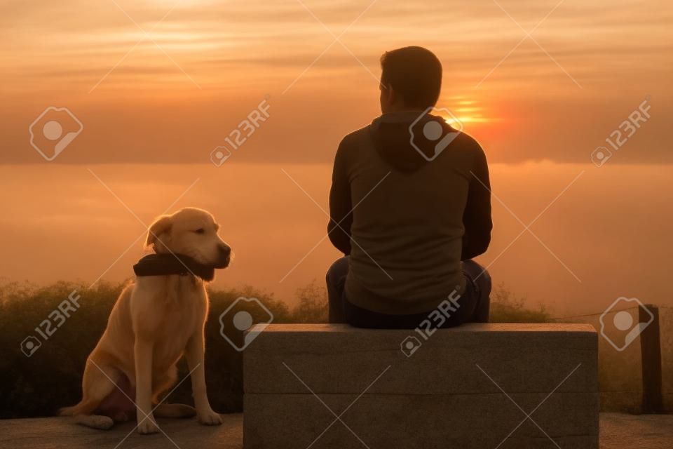 Giovane uomo con il suo cane al sorgere del sole.