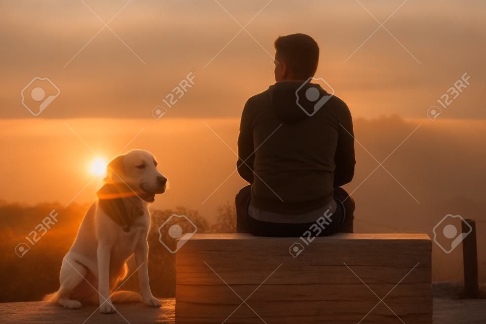 Giovane uomo con il suo cane al sorgere del sole.