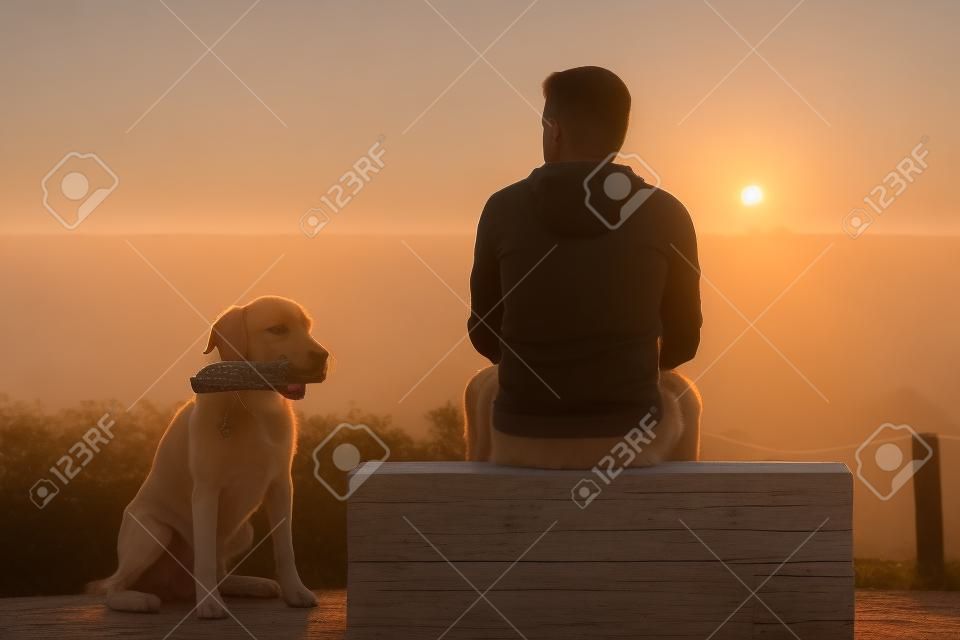 Jovem com seu cão ao nascer do sol.