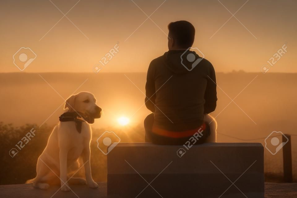 Junger Mann mit seinem Hund am Sonnenaufgang.