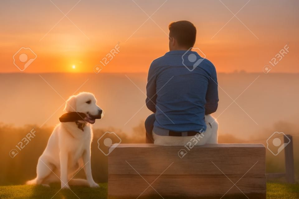 Junger Mann mit seinem Hund am Sonnenaufgang.