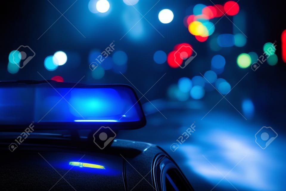 Niebezpieczeństwo na drodze. Błękitny migacz na samochodzie policyjnym przy nocą.