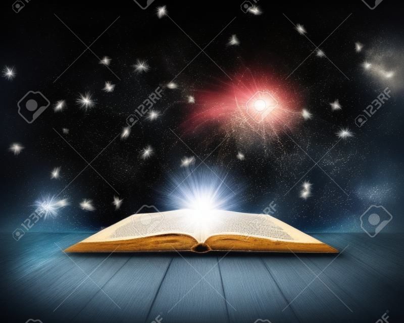 Old open book with magic light and falling stars  Dark background