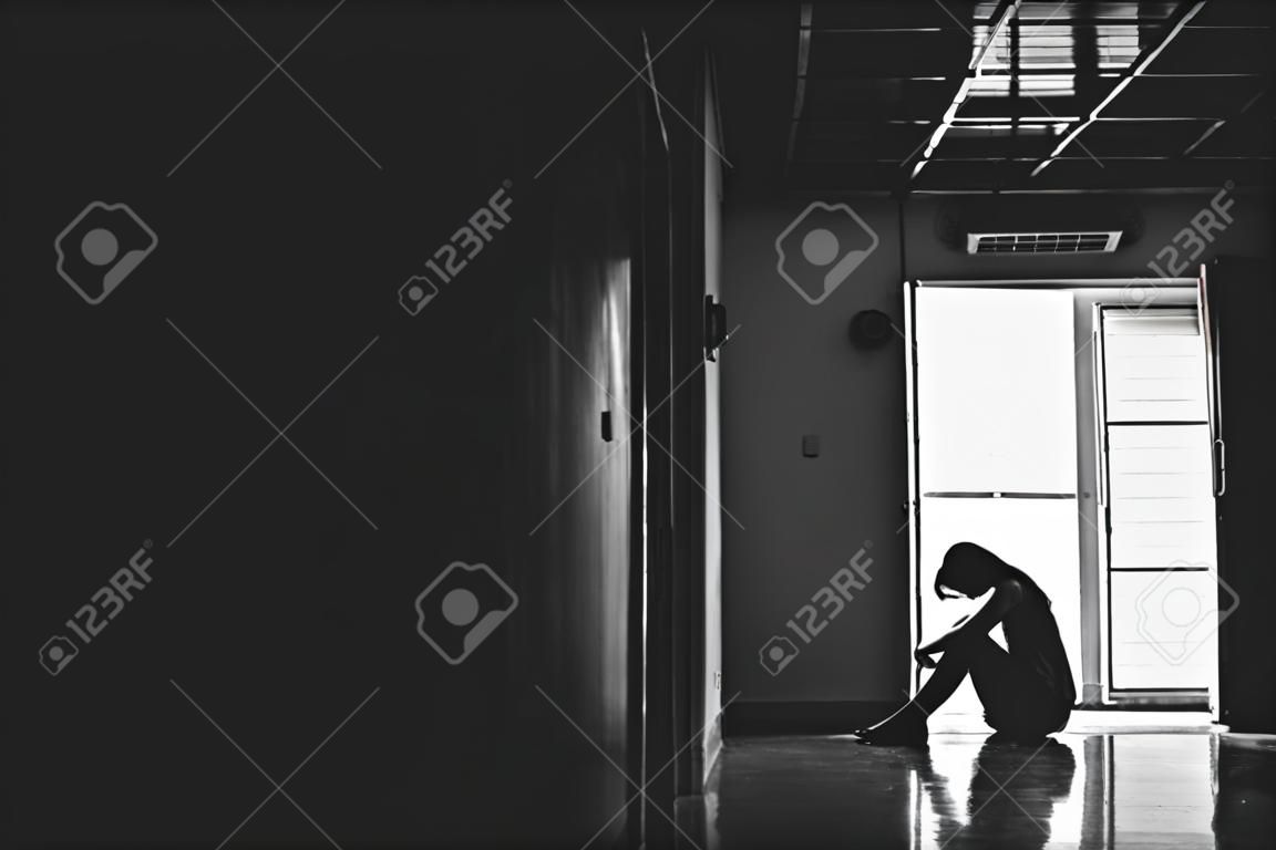 Sylwetka dziewczyny siedzącej samotnie w ciemności, smutne i poważne kobiety siedzące przytulić kolano samotnie do starego mieszkania, przemoc domowa, problemy rodzinne, stres, przemoc, pojęcie depresji i samobójstwa z miejscem na kopię