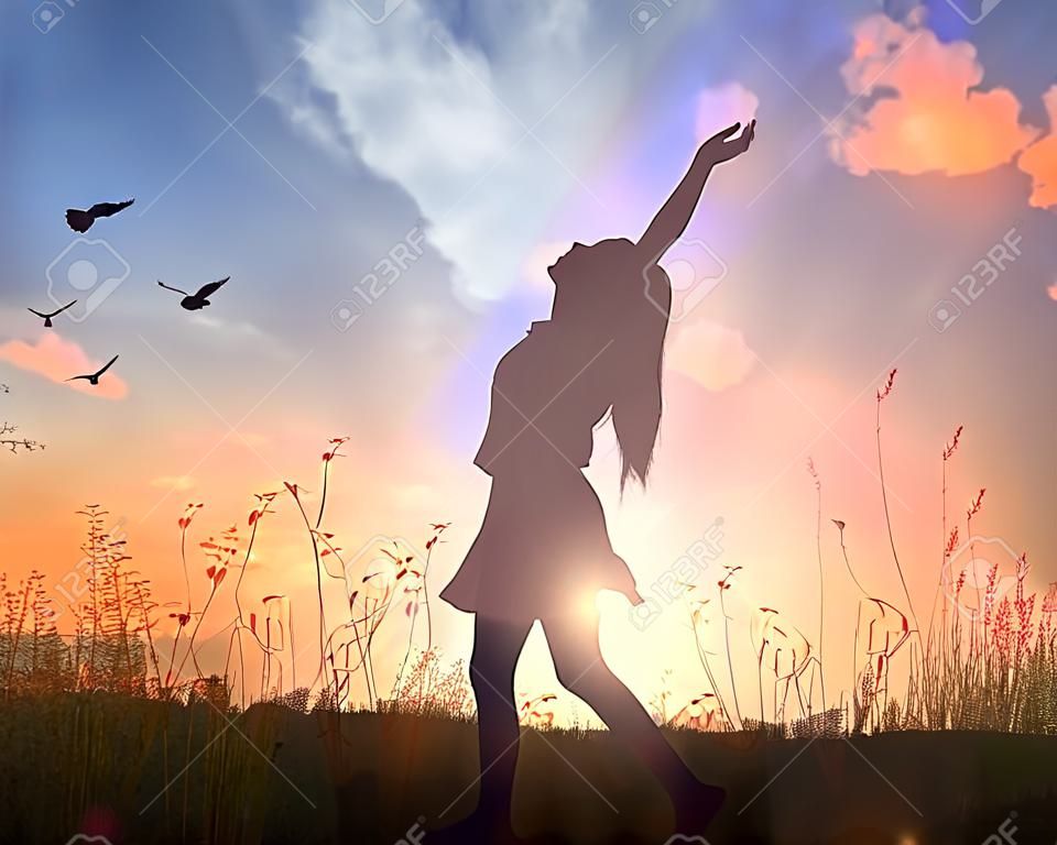 World mental health day concept: Silhouette of healthy woman raised hands for praise and worship God at autumn sunset meadow background