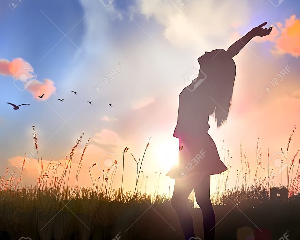 世界メンタルヘルスデーのコンセプト：秋の日没の牧草地の背景で神を賛美し、崇拝するために手を挙げた健康な女性のシルエット