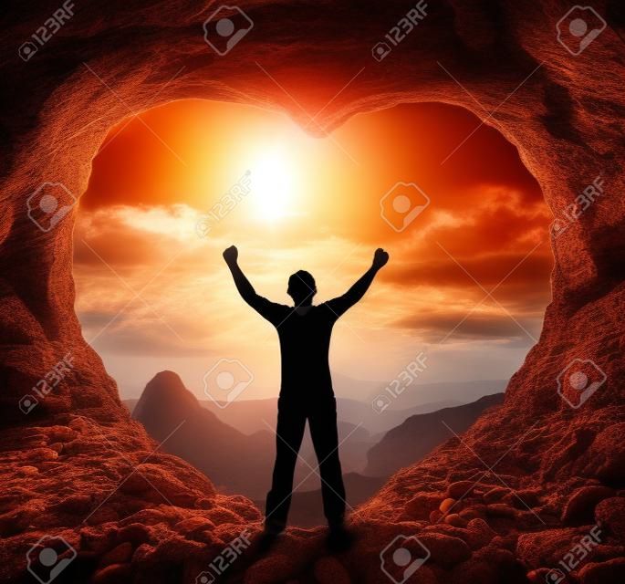 Conceito de deus de adoração: silhueta humana em pé na caverna do coração contra o fundo do nascer do sol da montanha