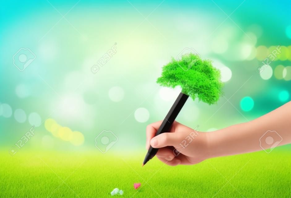 Concepto del día del maestro: mano del estudiante sosteniendo un lápiz de árbol y escribiendo en un prado verde sobre un fondo borroso del bosque