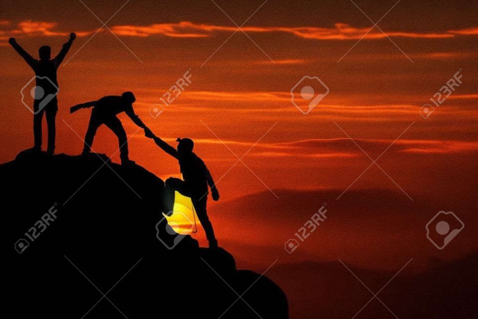 チームワークの友情のハイキングは、山、日の出の支援シルエットを信頼し合うのに役立ちます。登山チームの美しい日の出の風景の上で互いに助け合う2人の男性ハイカーのチームワーク