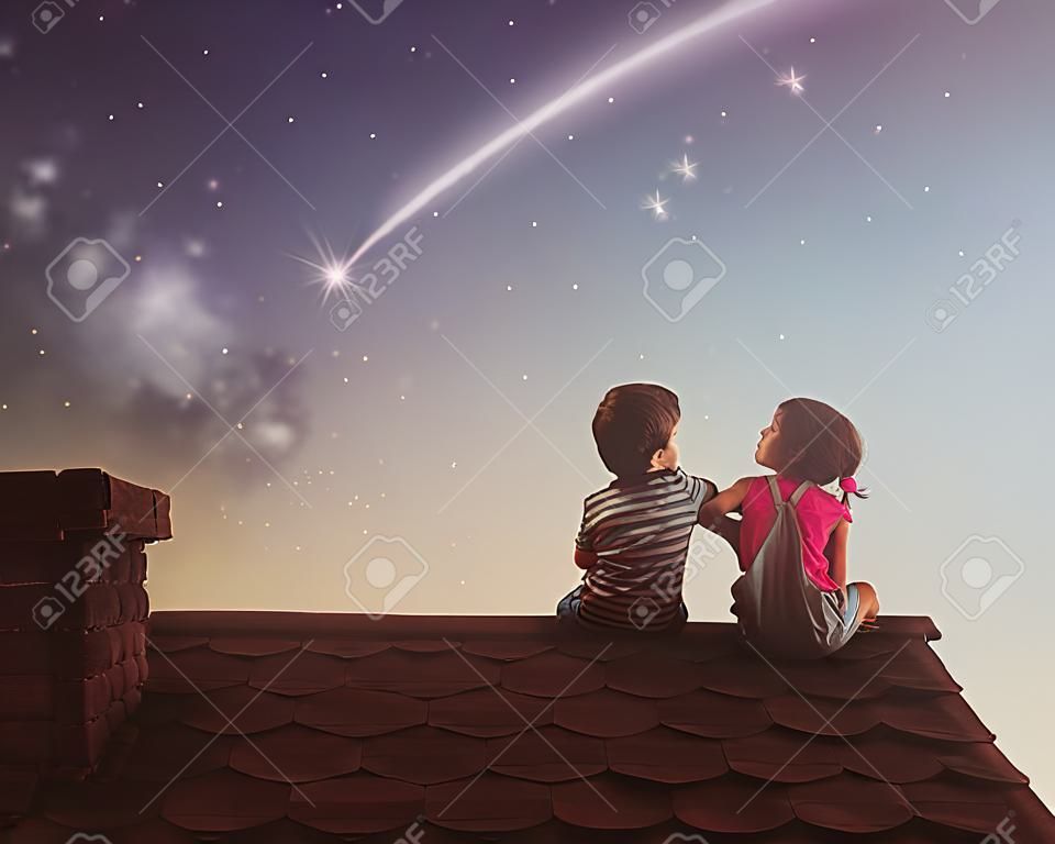 Dois filhos bonitos sentar no telhado e olhar para as estrelas. O menino e a menina fazem um desejo vendo uma estrela de tiro.