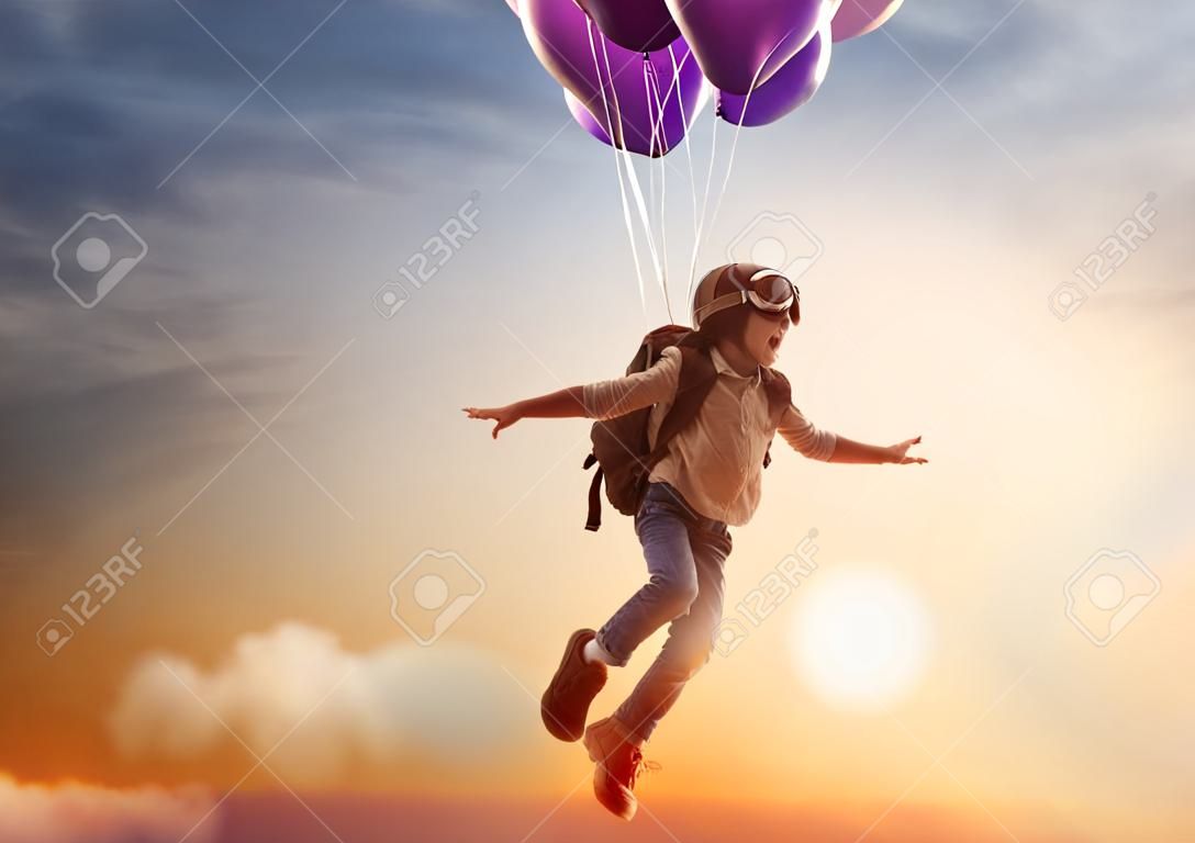 Sueños de viaje! Niño que vuela en los globos contra el telón de fondo de una puesta de sol.