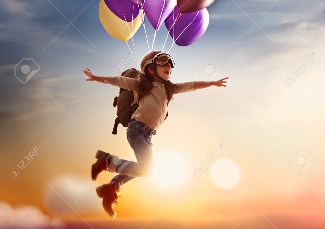 Dreams of travel! Child flying on balloons against the backdrop of a sunset.