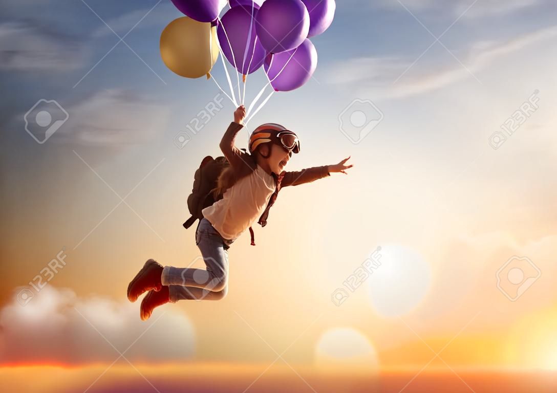 Sueños de viaje! Niño que vuela en los globos contra el telón de fondo de una puesta de sol.