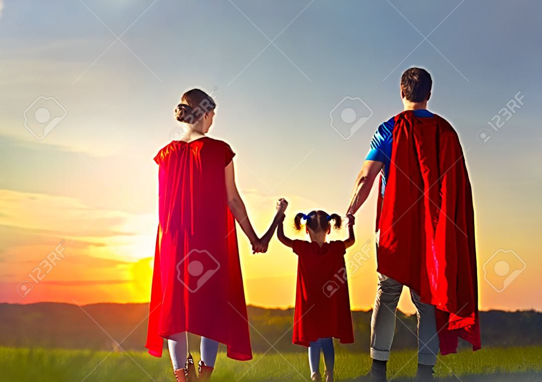 Mãe, pai e suas filhas estão brincando ao ar livre. Mamãe, papai e crianças meninas em fantasias de super-heróis. Conceito de super família.