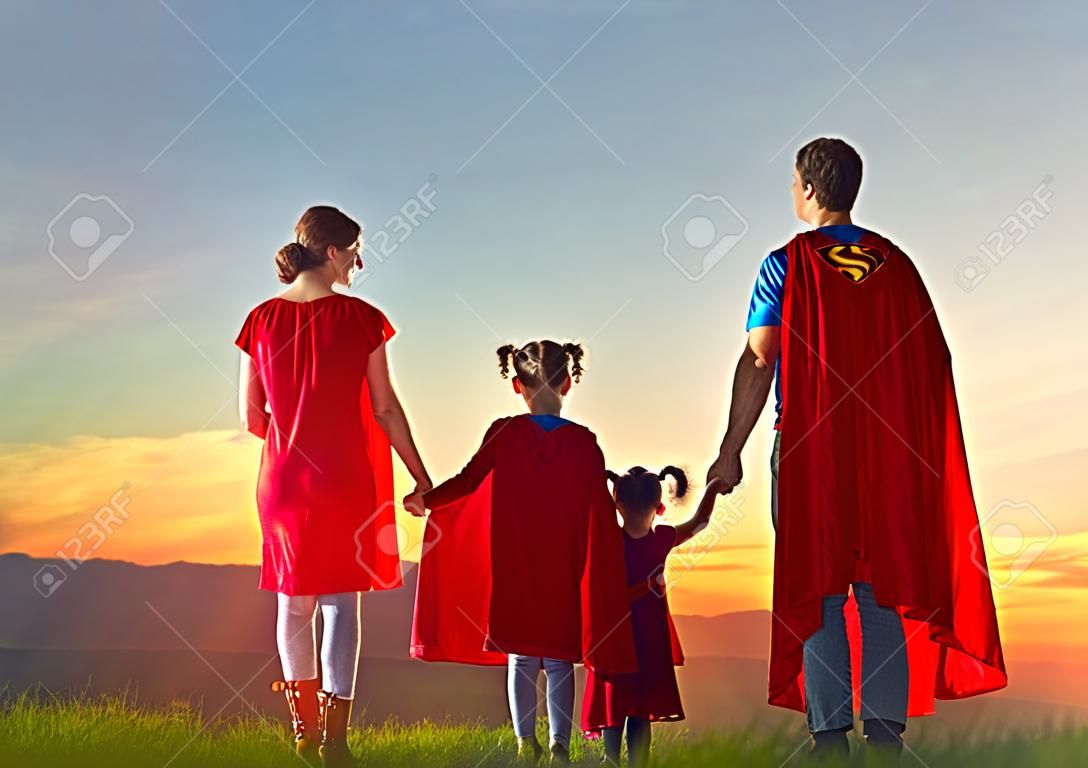 Mutter, Vater und ihre Töchter spielen im Freien. Mama, Papa und Kinder Mädchen in einem Kostüm des Superhelden. Konzept der Superfamilie.
