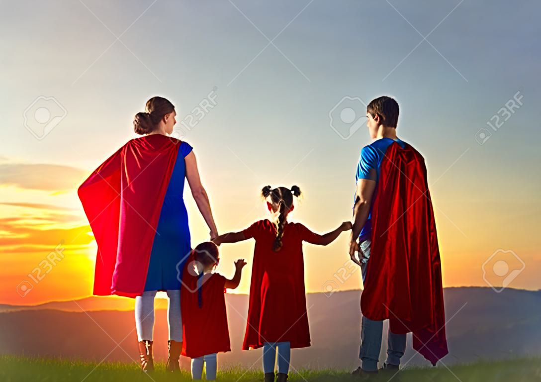 Madre, padre e le loro figlie stanno giocando all'aperto. Mamma, papà e bambini ragazze in costume di un supereroe. Concetto di super-famiglia.