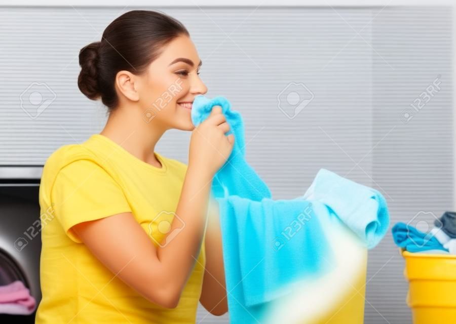 美丽的年轻女子在家里洗衣服时，闻到了干净的衣服和微笑。