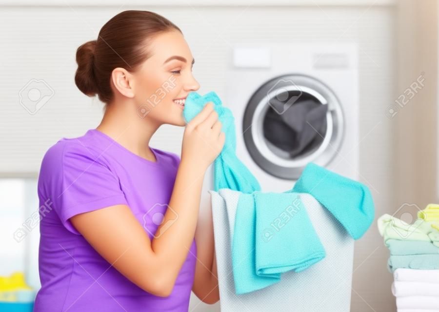 美丽的年轻女子在家里洗衣服时，闻到了干净的衣服和微笑。