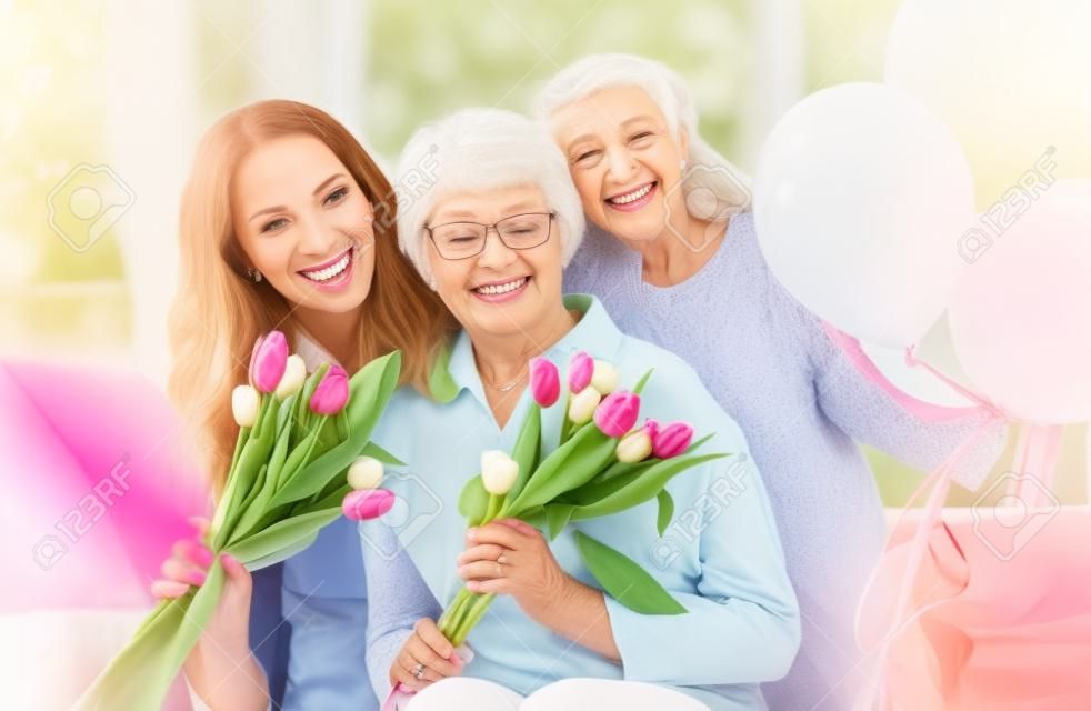 Happy mother's day! Child daughter is congratulating mom and granny giving them flowers tulips. Grandma, mum and girl smiling and hugging. Family holiday and togetherness.