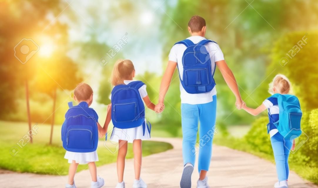 Padres y alumnos de primaria van de la mano. Hombre y niñas con mochilas a la espalda. Inicio de lecciones. Primer día de otoño.