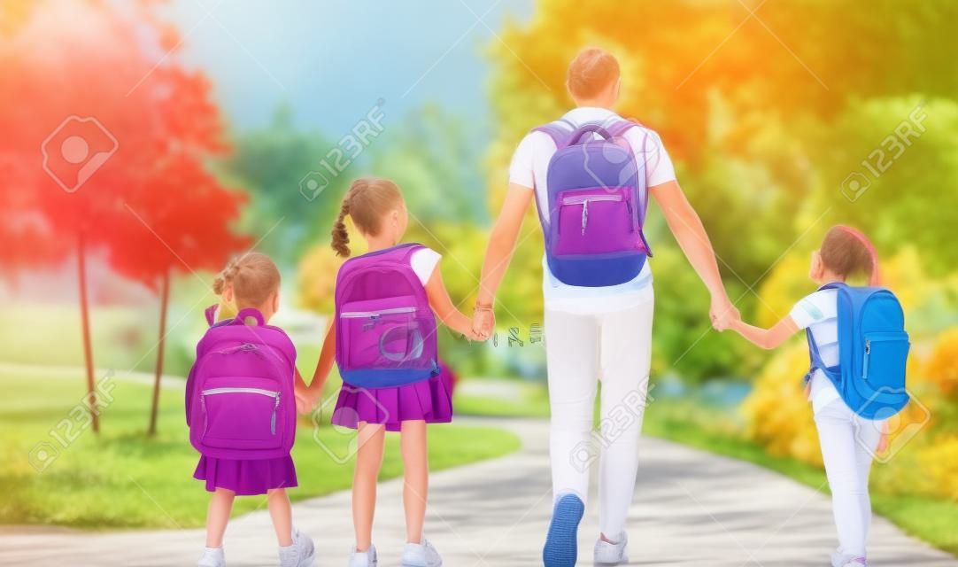 Genitori e alunni della scuola primaria vanno di pari passo. Uomo e ragazze con zaini dietro le spalle. Inizio delle lezioni. Primo giorno d'autunno.