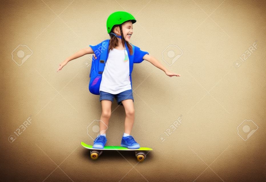 子供の頃と幸せな時間！カラー紙の壁の背景にスケートボードとかわいい子。バックパック付きの子供。勉強する準備ができている女の子。