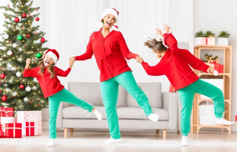 Merry Christmas, Happy Holidays. Cheerful mom and her cute daughters girls are dancing. Parent and little children having fun near tree indoors.