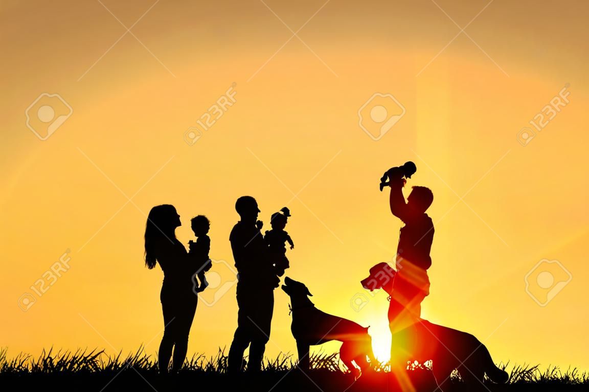 Sylwetka szczęśliwa rodzina czterech ludzi, matka, ojciec, dziecko, i dzieci, i ich pies z przodu na zachód słońca nieba, z miejsca na tekst lub miejsca kopii