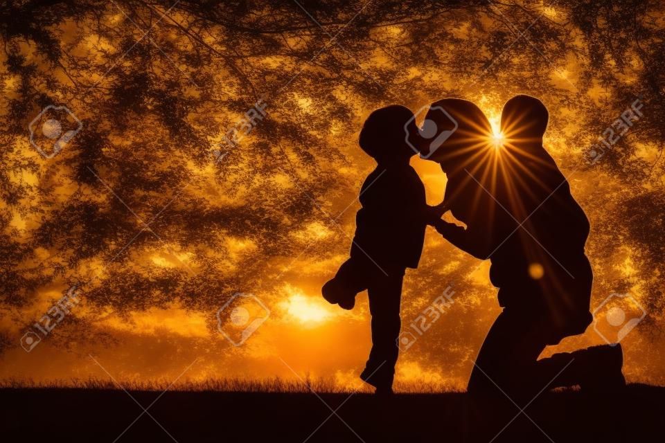 一位母親和她的兩個年幼的孩子的剪影;一個小男孩和他的弟弟在日落都在外面玩，擁抱和親吻。
