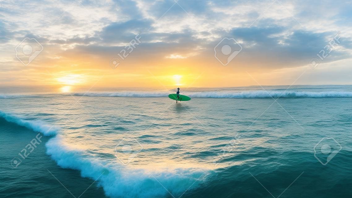 Surfer athlete enters beach ocean shallow waters to paddle out through ocean waves to go surfing at morning sunrise .