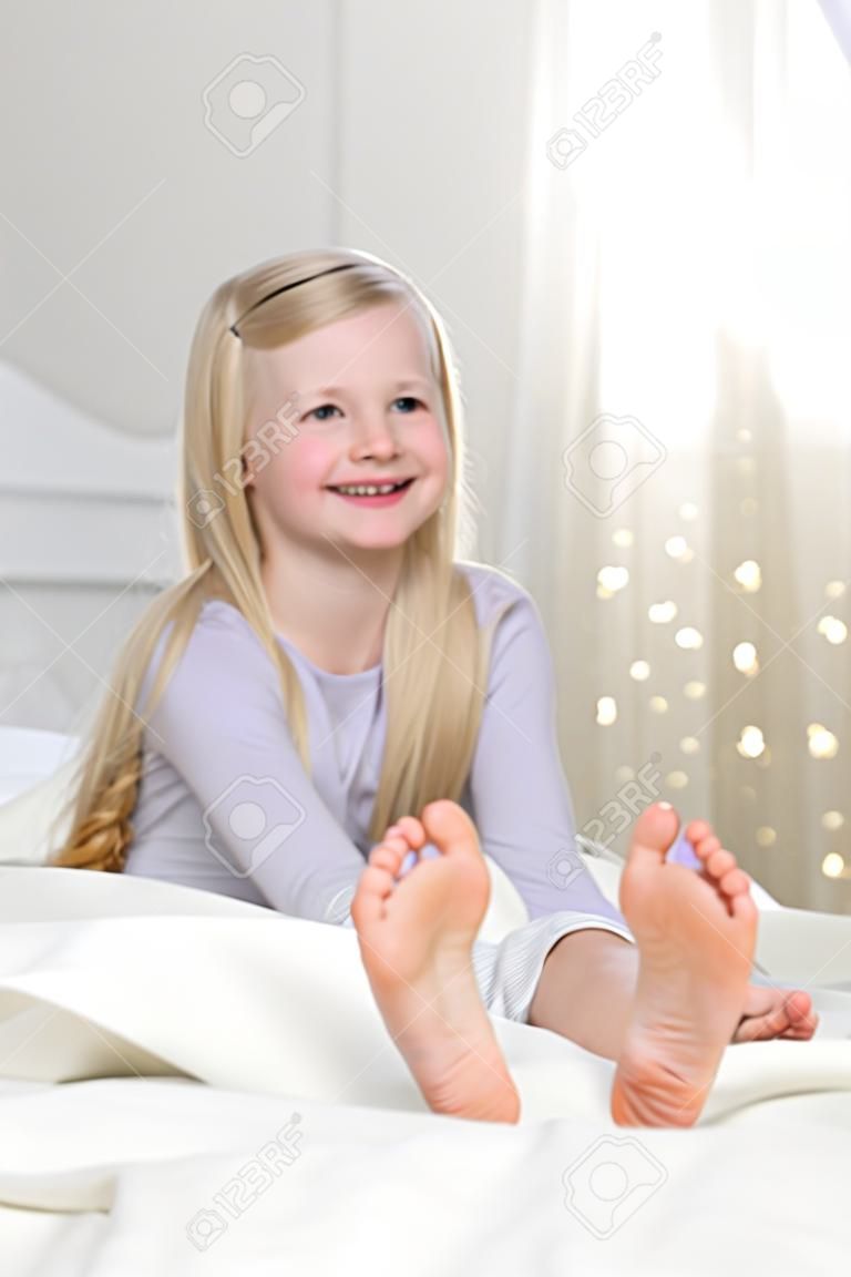 Bonne fille blonde est assise pieds nus dans le lit