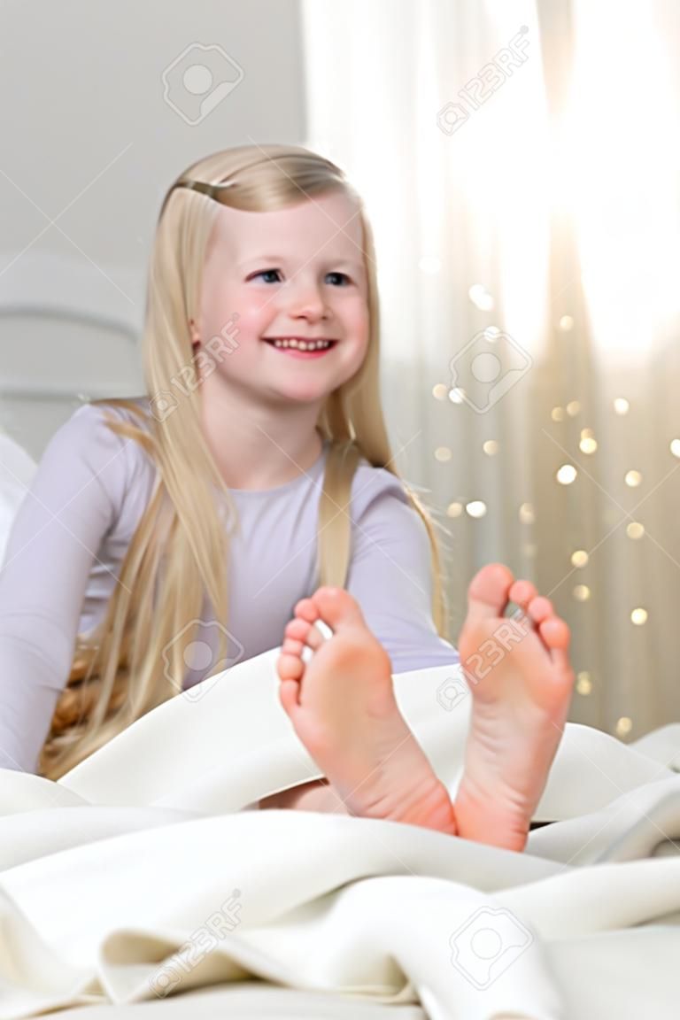 Bonne fille blonde est assise pieds nus dans le lit