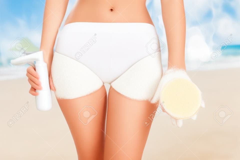 Young woman on the beach is holding brush and cream in hands antu cellulite treatment. Cellulite problem concept.