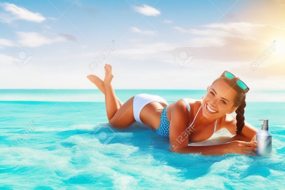 太陽吻了美。快樂活躍的女人在泳衣在海濱與防曬霜