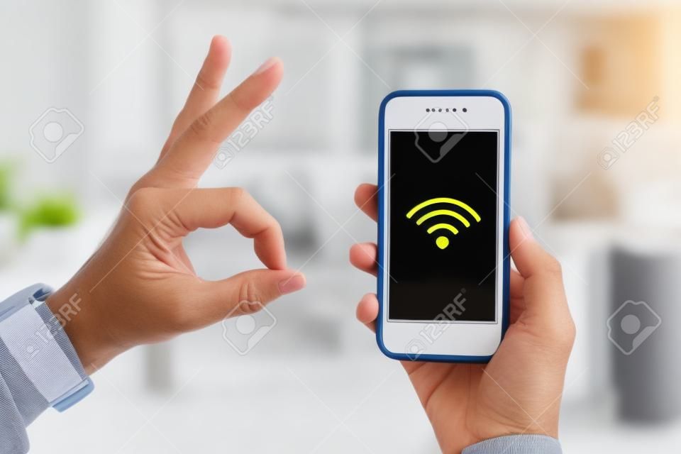 Closeup on smartphone with strong wifi signal in hand of modern housewife and other hand showing ok gesture in the house.