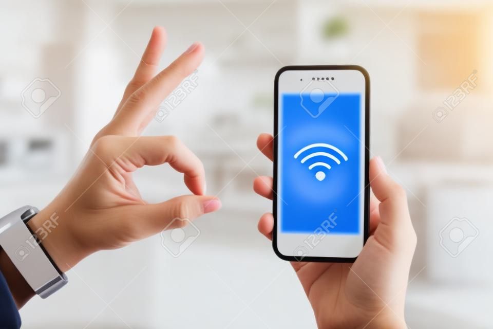 Closeup on smartphone with strong wifi signal in hand of modern housewife and other hand showing ok gesture in the house.