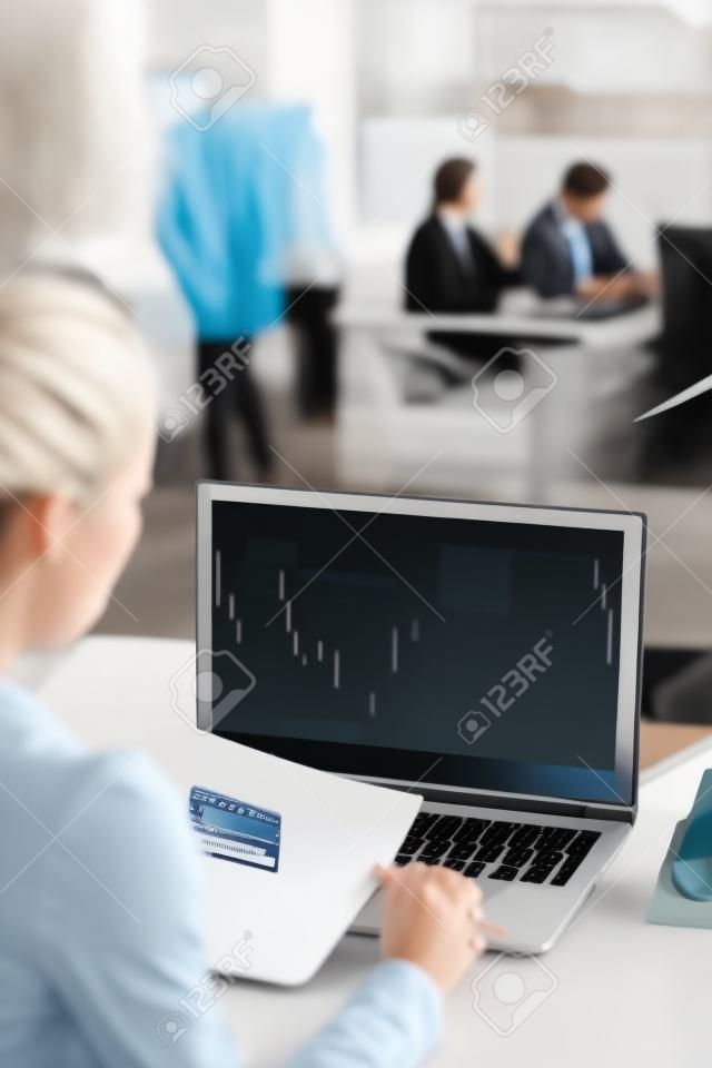 Seen from behind modern woman with laptop checking financial information in modern office.